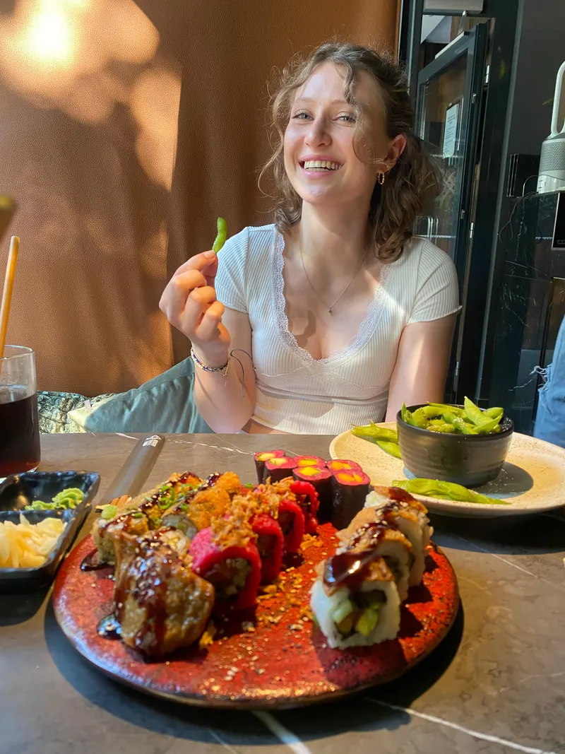 Emily lächelt bei einem Restaurantbesuch mit Sushi und Edamame.